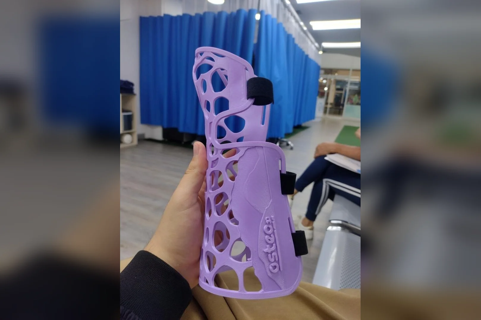 3D printed lavender arm orthosis with velcro straps, printed as an earthquake relief item, held up in a Venezuelan clinic